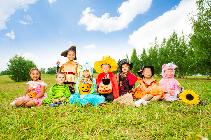 Happy kids in Halloween costumes sit on grass