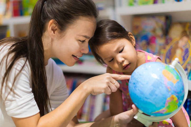 A teacher and a preschool student learning geography on a world globe